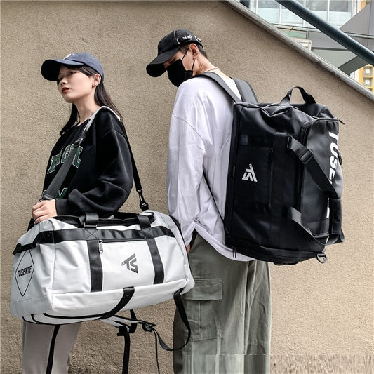 Two people with bags, one holding a white and black duffel bag, the other with a black backpack, against a beige wall.