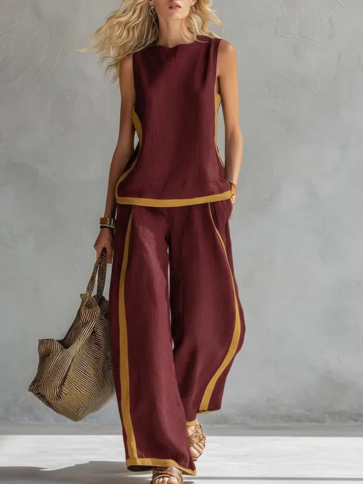 Woman wearing a burgundy outfit with gold trim, holding a textured bag against a neutral background.