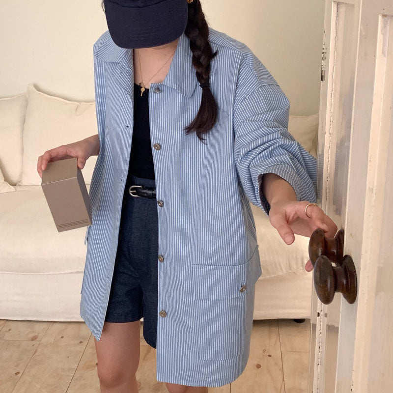 Person wearing a blue striped shirt over a black outfit, holding a box in a room with a couch.