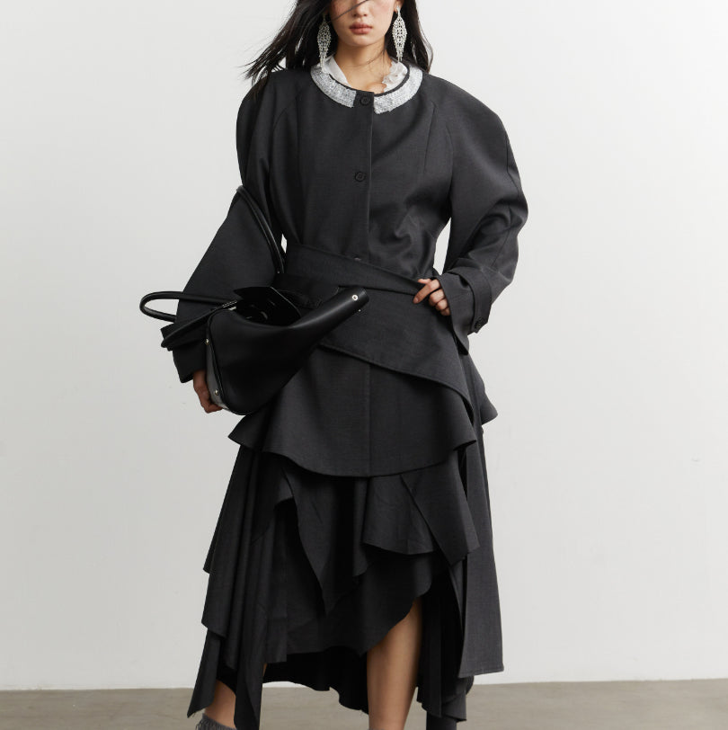 Person wearing a black layered outfit with a white collar against a plain background