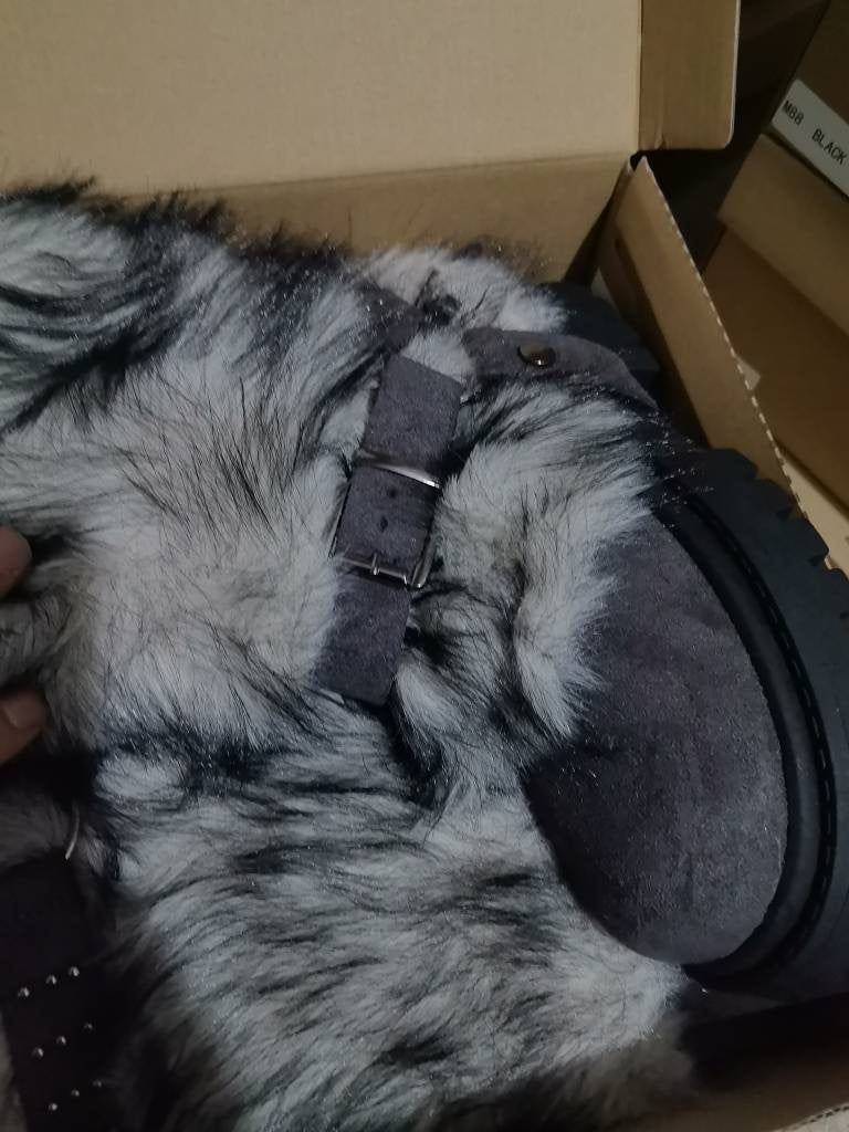 Gray and black fur-lined ear muffs with a strap on a cardboard surface.