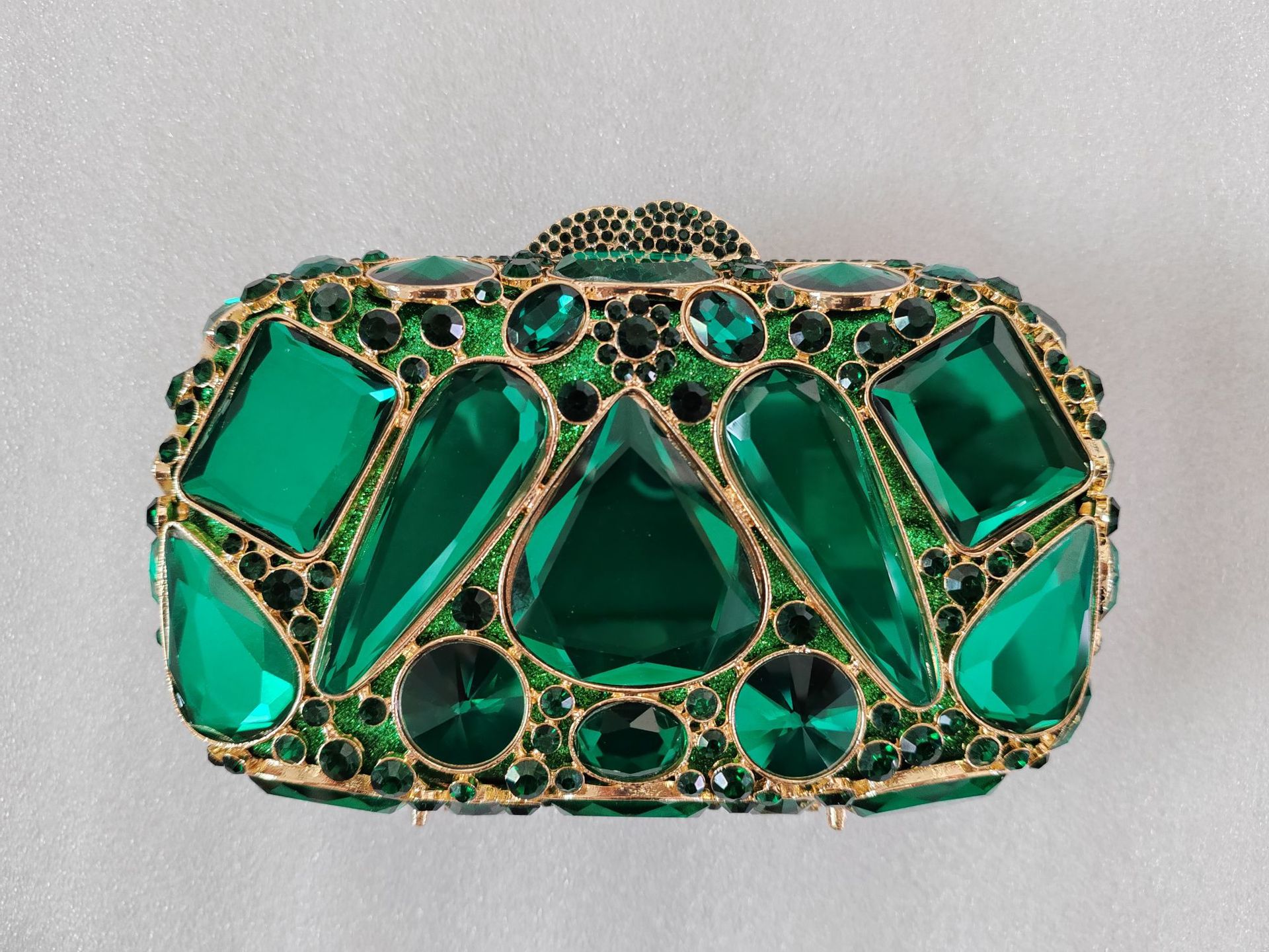 Green gemstone clutch bag with gold accents on a light gray background