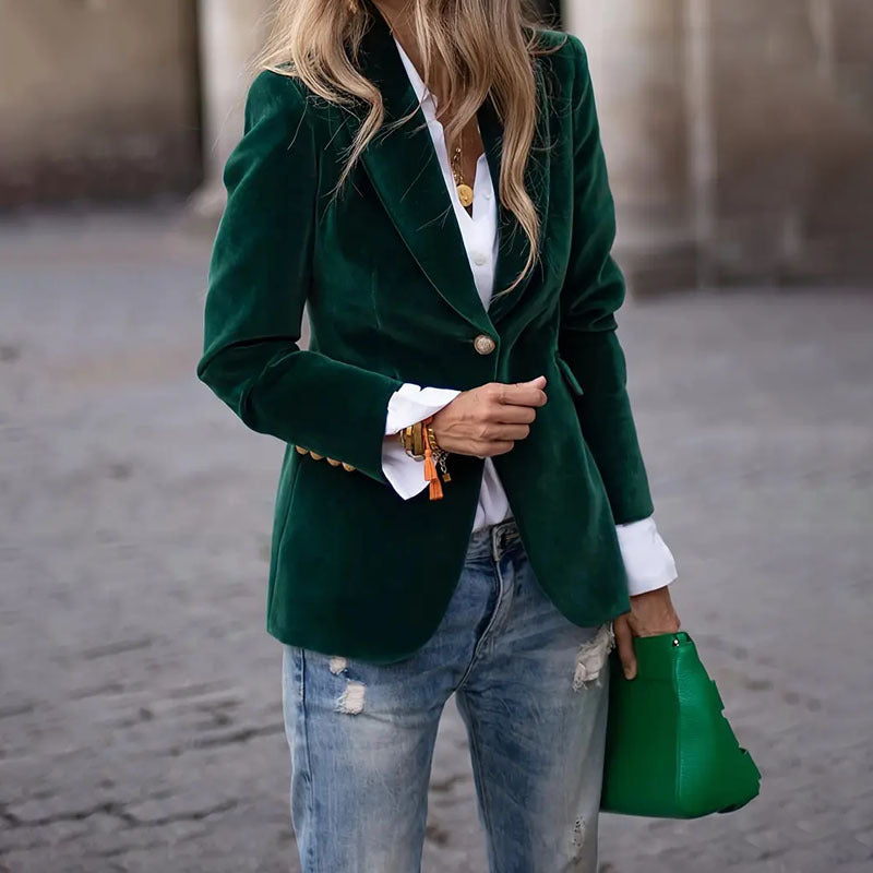Person wearing a green blazer, white shirt, and blue jeans, holding a green handbag.