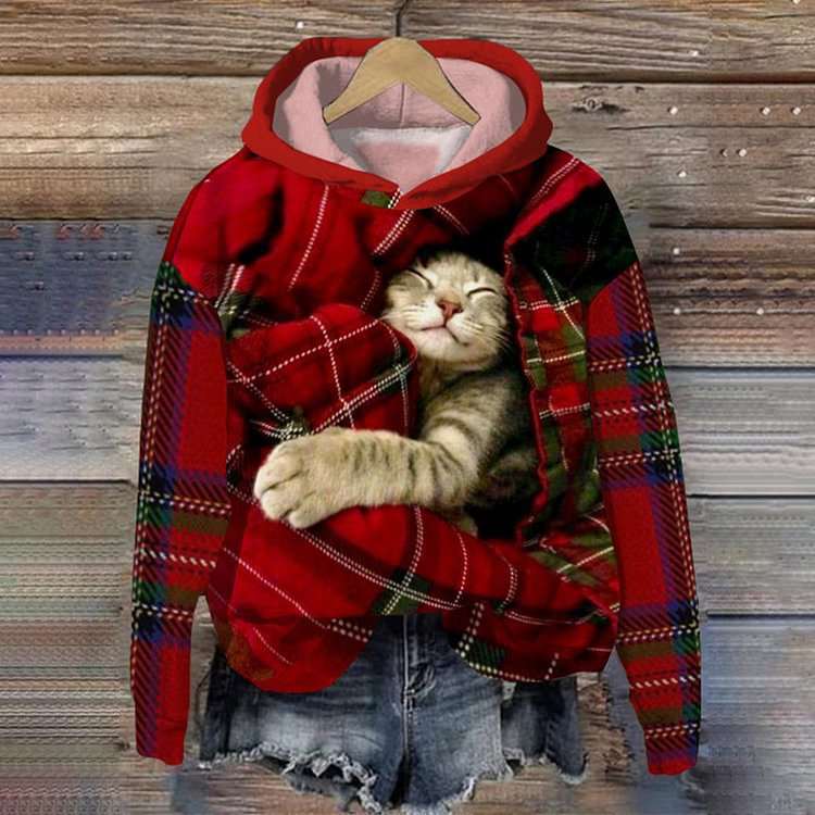 Cat sleeping inside a red plaid hoodie on a wooden background