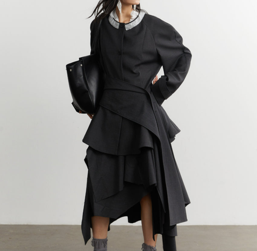 Person wearing a black layered outfit with a white collar against a plain background