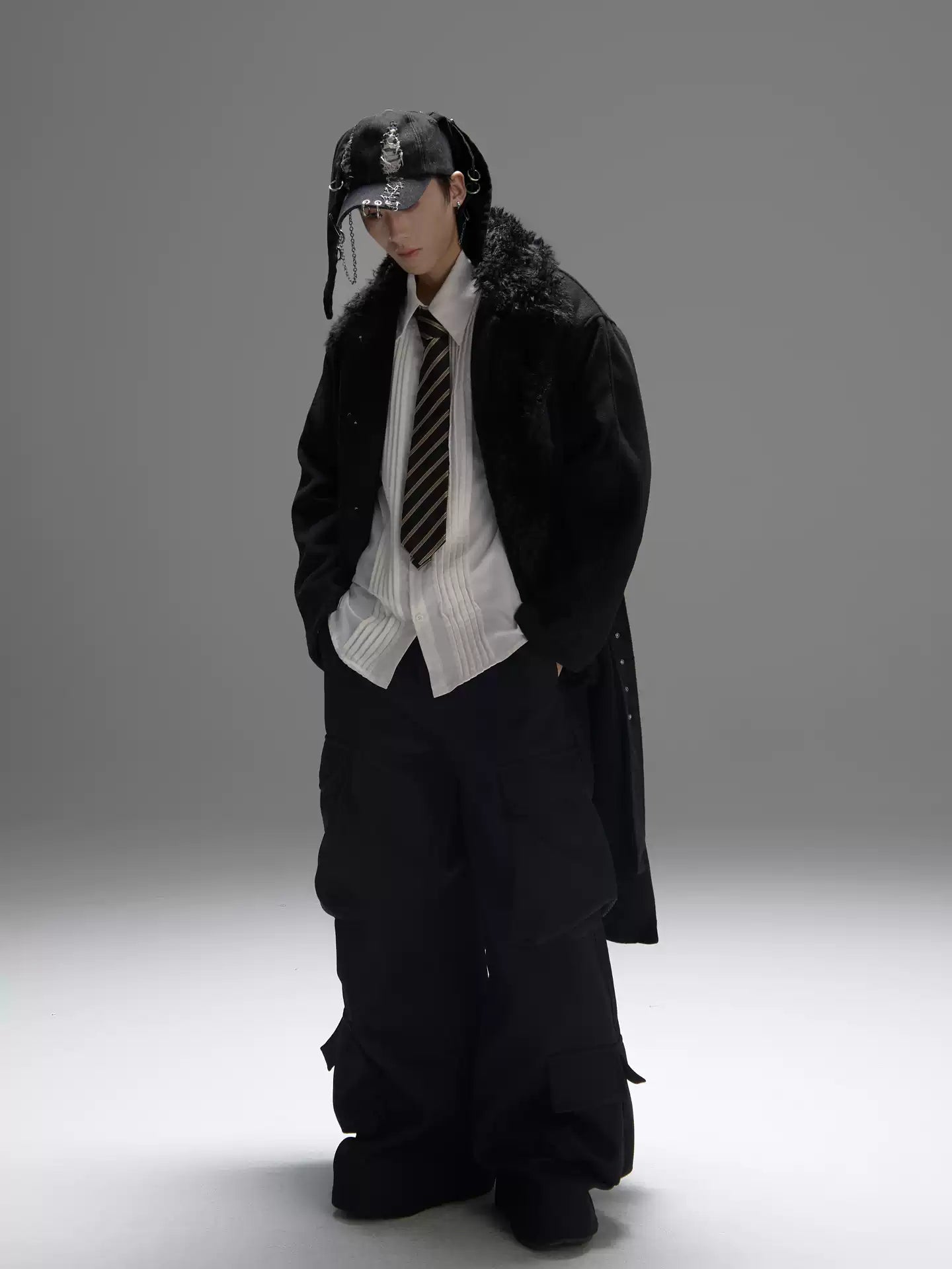 Person wearing a long black coat, white shirt, and tie on a gray background