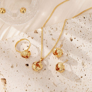 Gold jewelry set including necklace, ring, and earrings on a textured beige surface