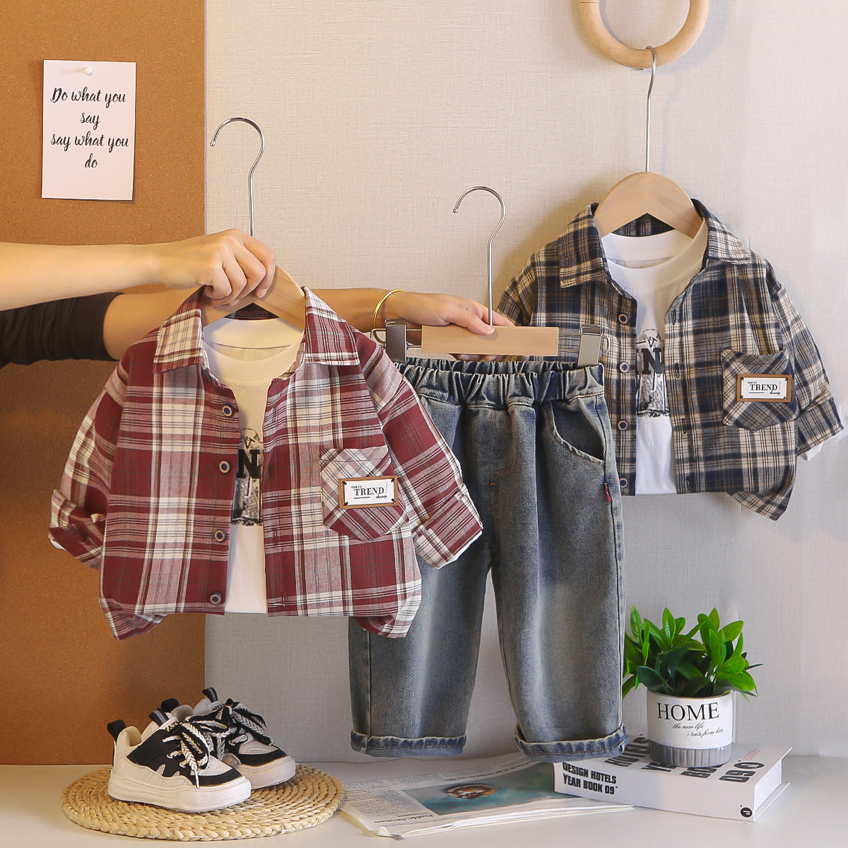 Two children's outfits on hangers with a plant and books in the background.