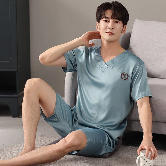 Man wearing a light blue satin pajama set sitting on the floor.