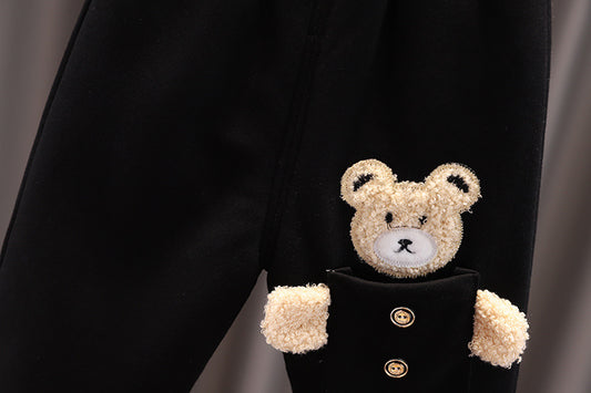 Teddy bear peeking out from a black coat with gold buttons on a gray background
