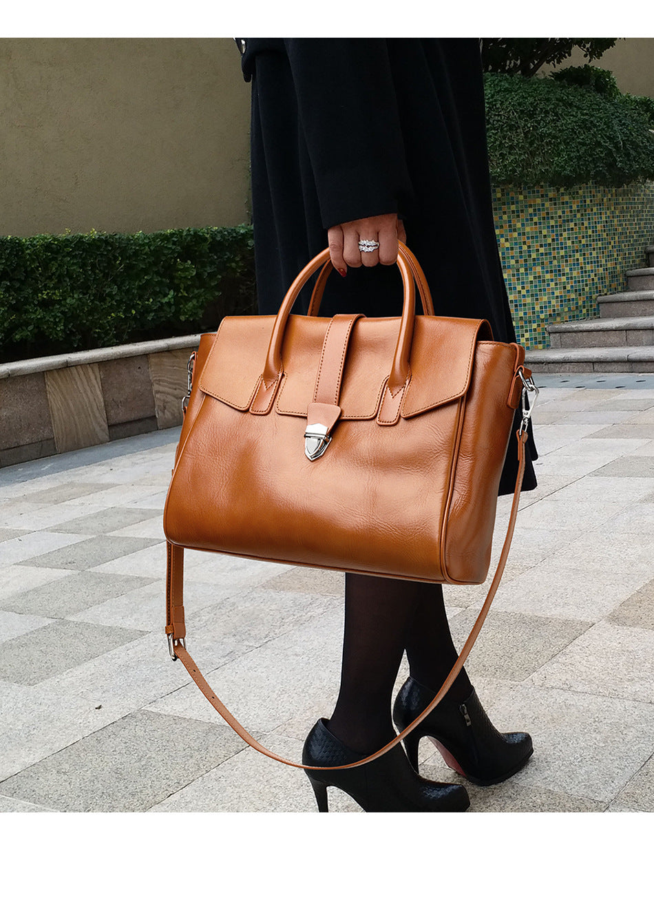 Person holding a brown leather handbag on a sidewalk.