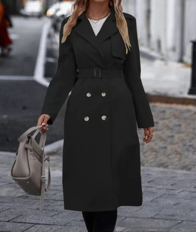 Person wearing a black trench coat walking on a city street.