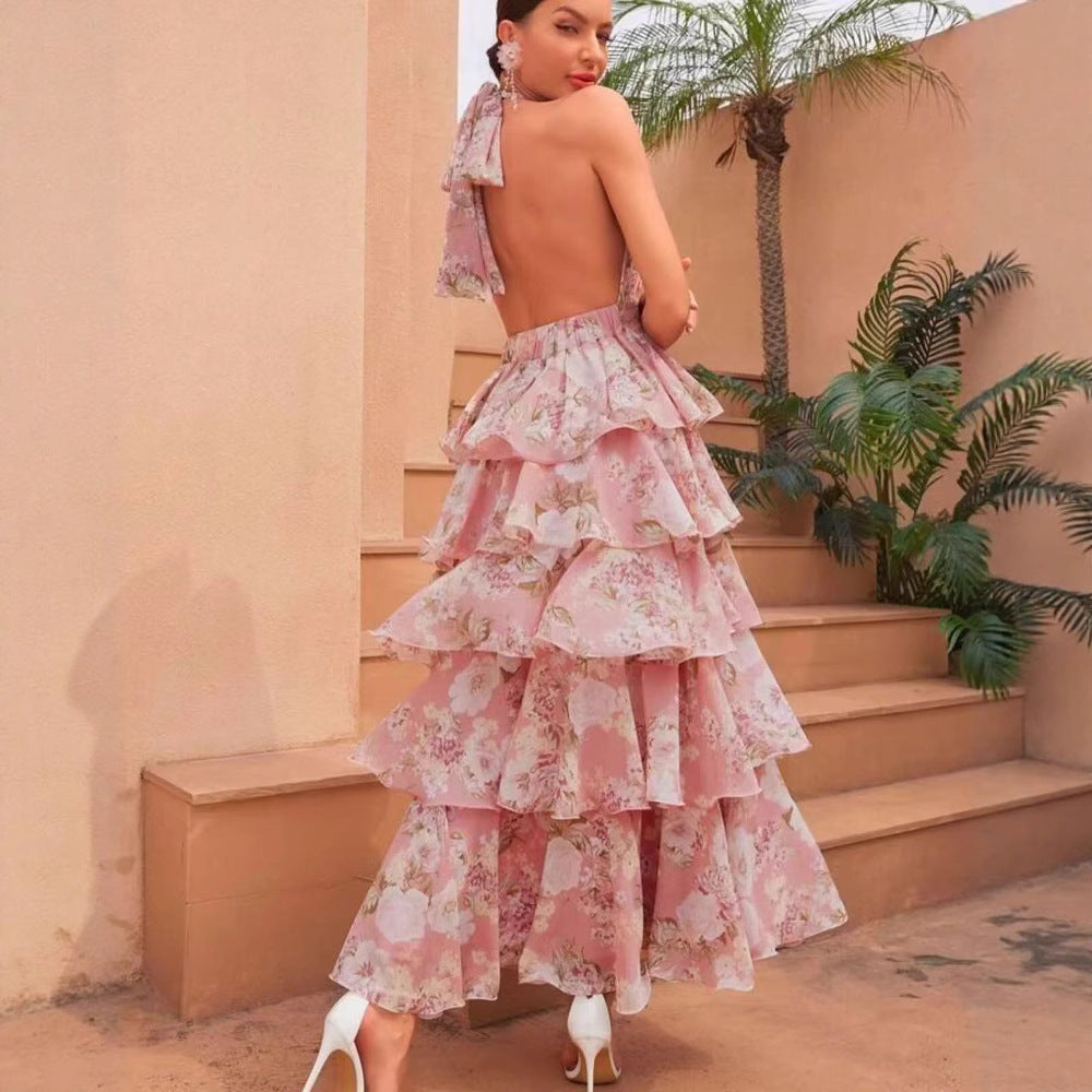 Woman in a pink floral dress standing on steps with a beige wall and plants in the background