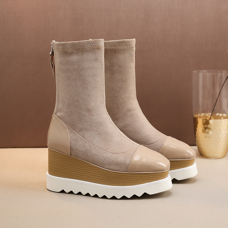 Pair of beige ankle boots with brown platform sole on a beige surface.