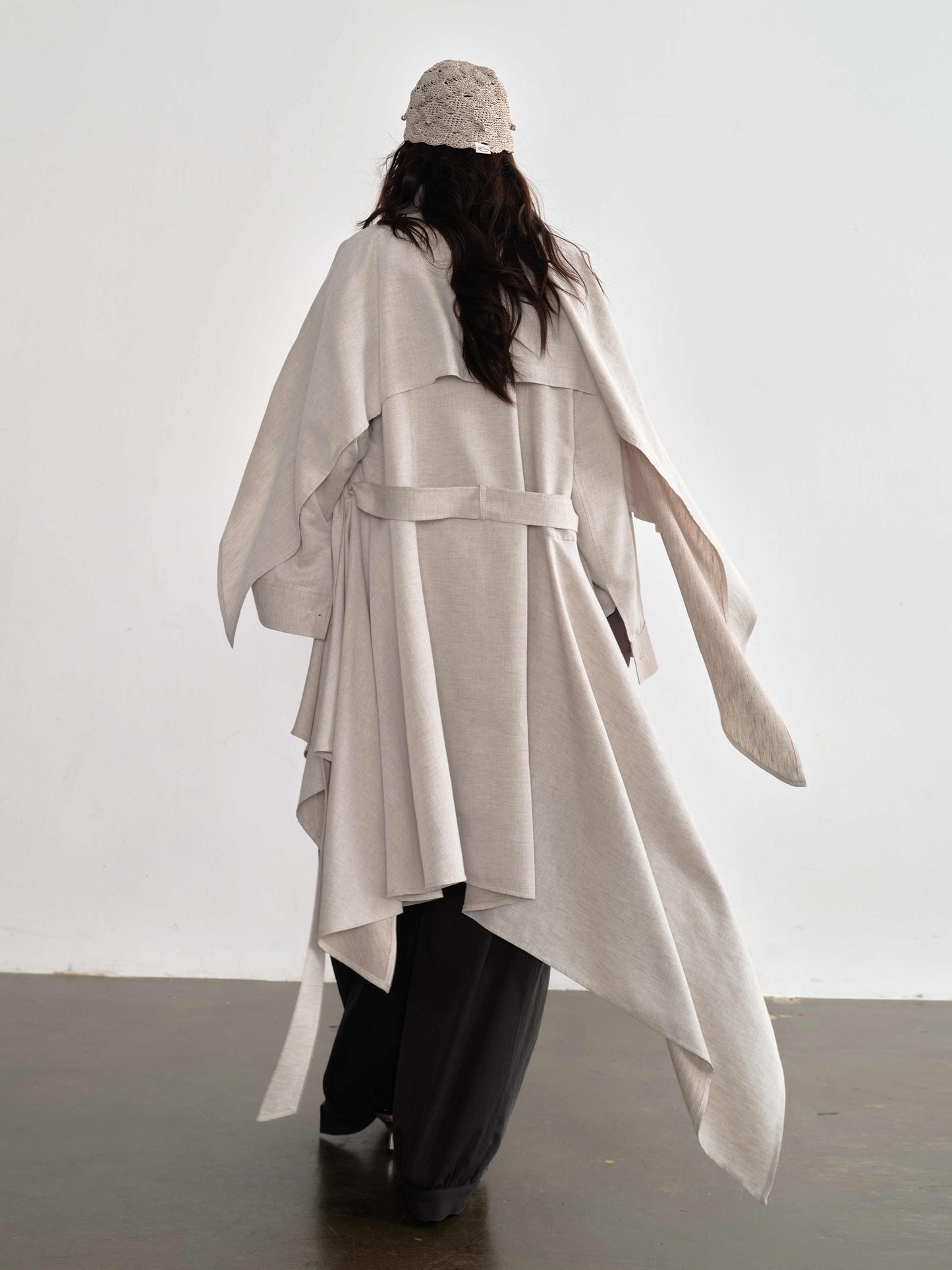 Person wearing a long, light-colored coat with a belt against a white background