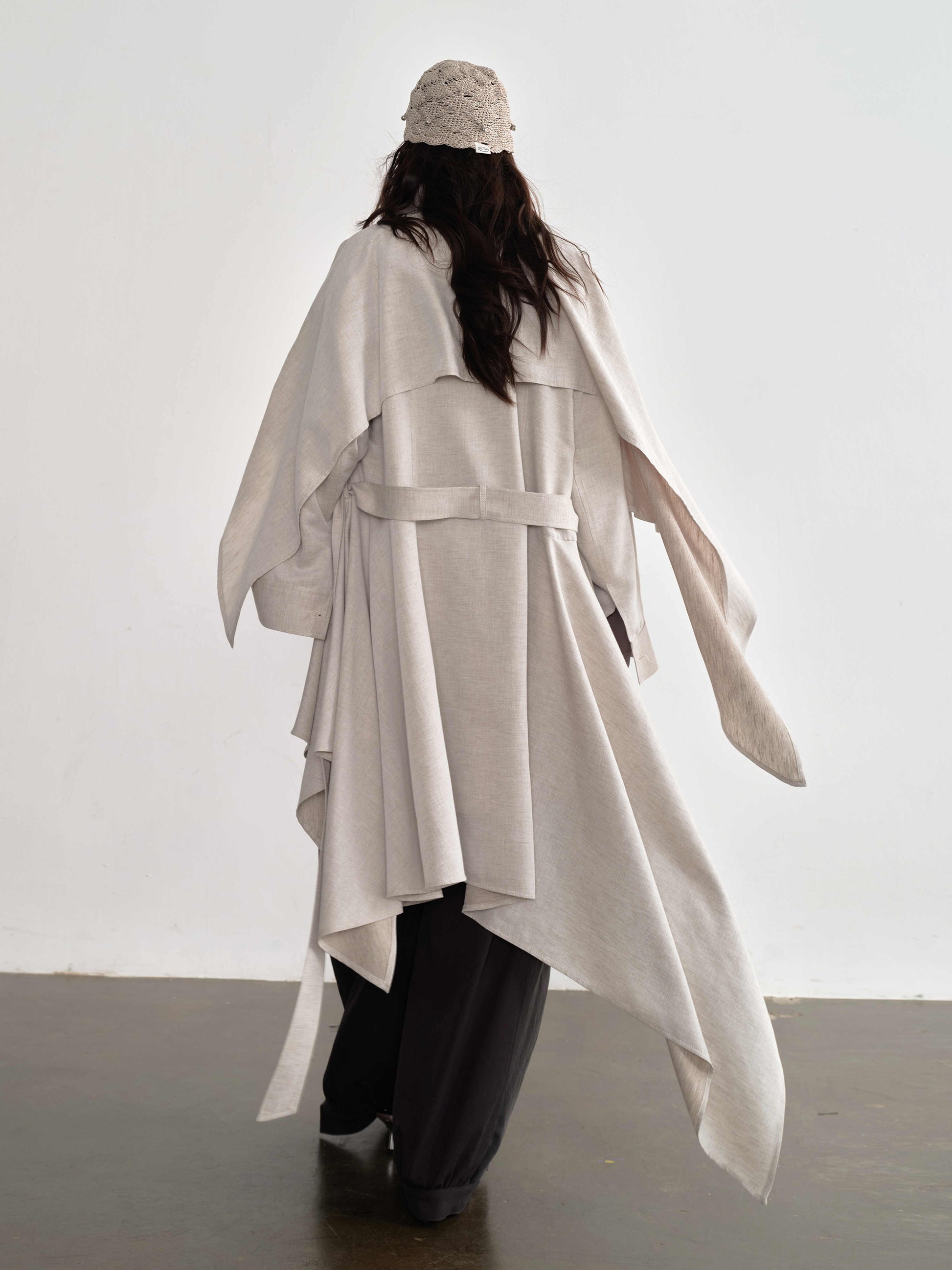 Person wearing a long, light-colored coat with a belt against a white background