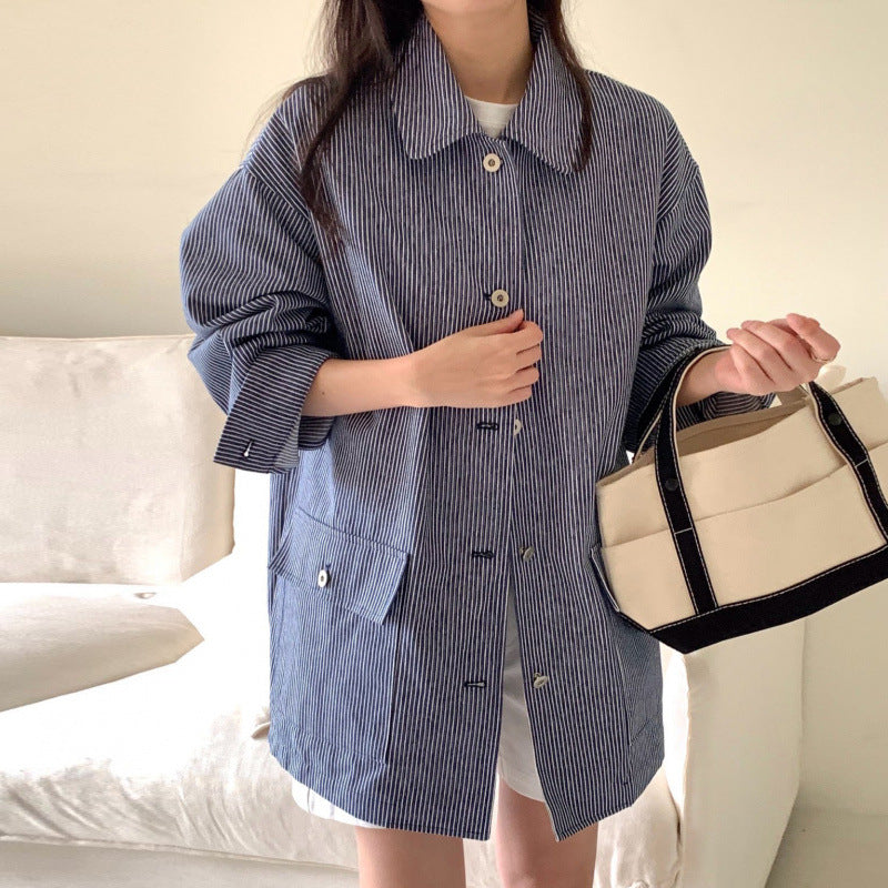 Person wearing a blue striped shirt over a white dress, holding a beige handbag.