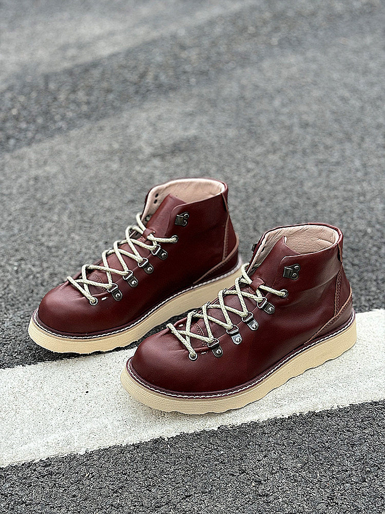 Pair of maroon boots with white soles on a gray asphalt surface.