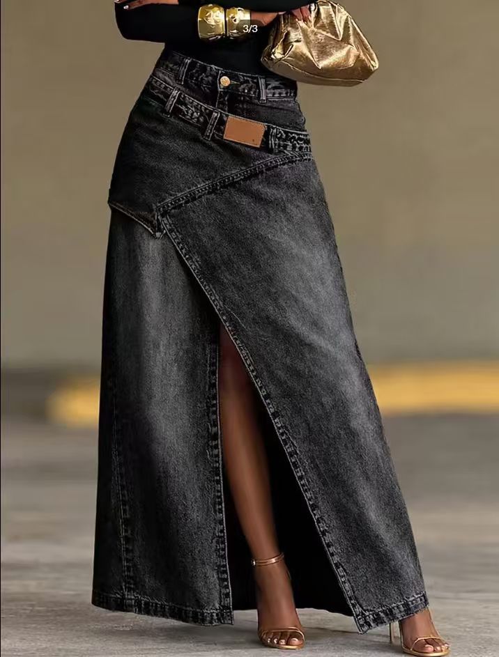 A woman models a long, dark gray denim wrap skirt with a high side slit, paired with a black top, metallic gold accessories, and gold high-heeled sandals.