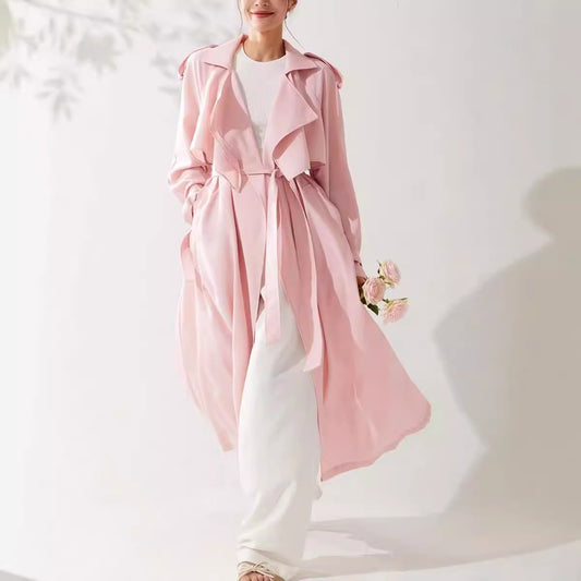 Person wearing a pink trench coat over a white outfit on a light background