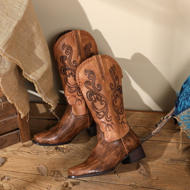 Pair of brown cowboy boots with intricate designs on a wooden floor.