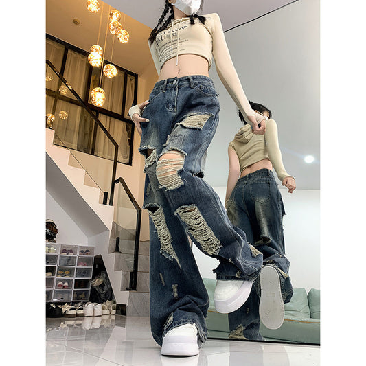 Person wearing ripped jeans and a beige crop top in a modern interior setting.