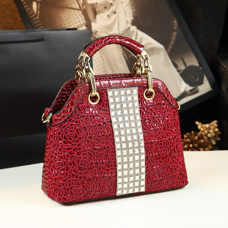Red handbag with intricate design and rhinestone strip on a blurred background