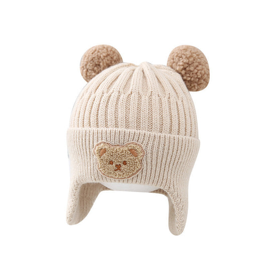 Beige knit baby hat with bear design and pom-poms on a white background