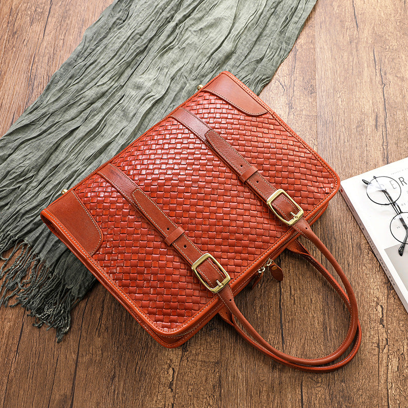 Brown woven handbag with gold buckles on a wooden surface with a gray scarf and white card.