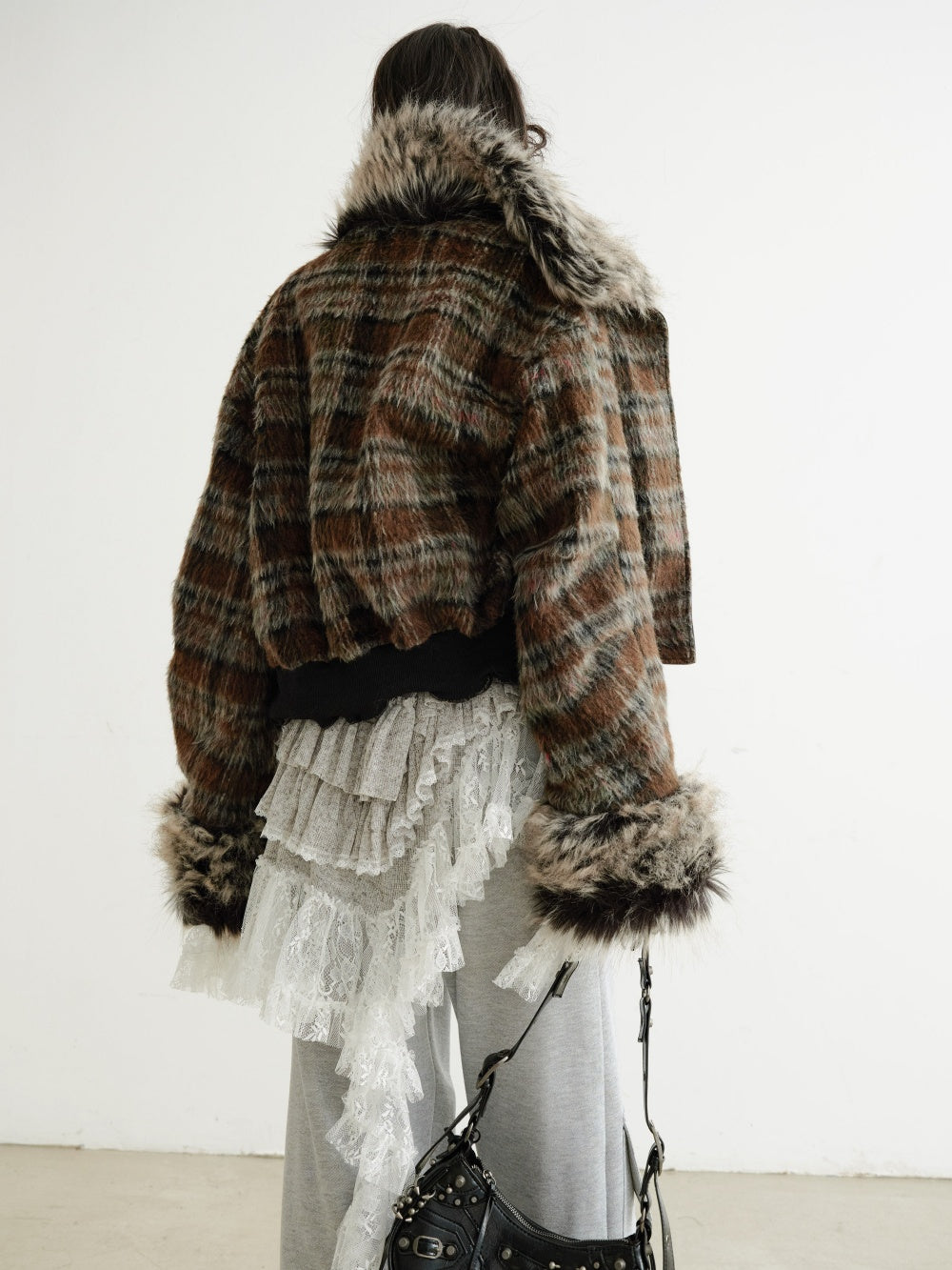 Person wearing a plaid coat with fur trim and a layered outfit on a plain background