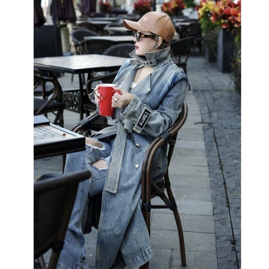 Person wearing a denim jacket and jeans sitting outdoors with a red cup.