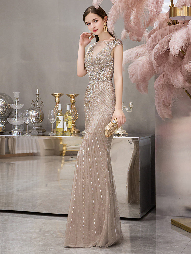 Woman in a beaded evening gown standing in an elegant room with decorative elements.