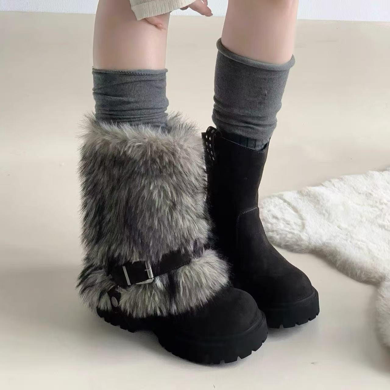 Black boots with fur trim worn by a person on a light background