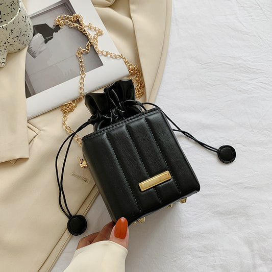 Black handbag with gold accent held by a hand on a white surface