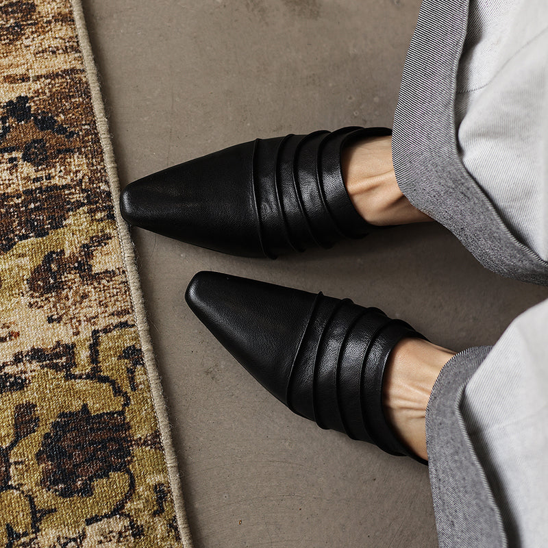 Black pointed-toe shoes worn by a person on a textured floor.