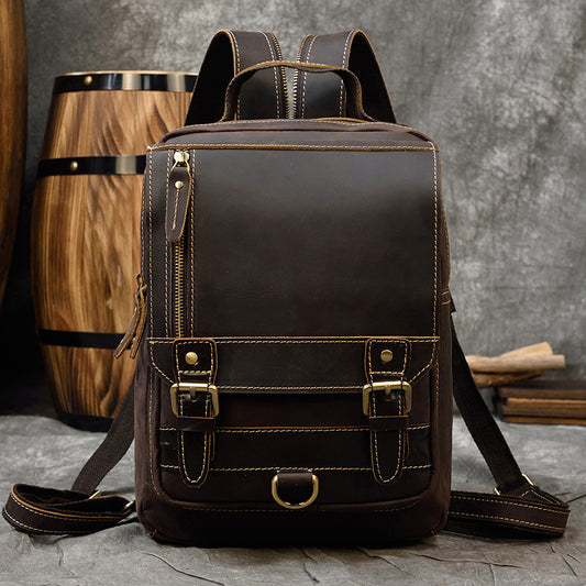 Brown leather backpack with gold buckles on a gray surface with a wooden barrel in the background
