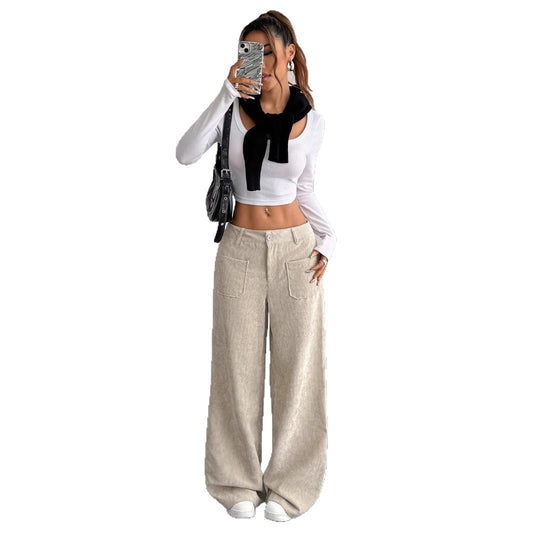 Person wearing a white long-sleeve top with a black bow, beige wide-leg pants, and white sneakers on a white background.