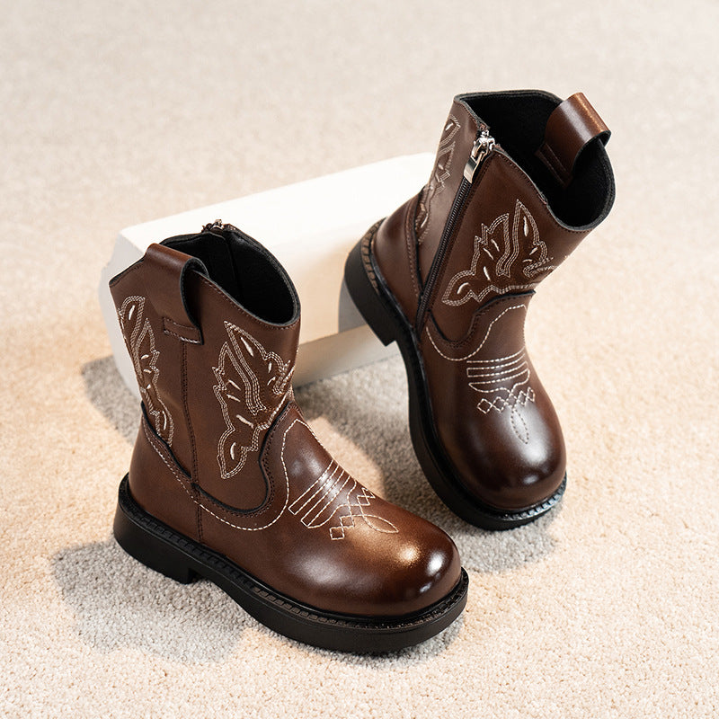 Pair of brown leather boots with decorative stitching on a beige surface
