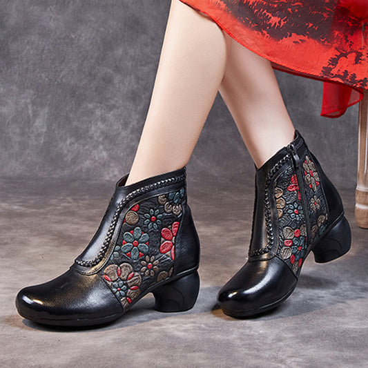 Black ankle boots with floral embroidery worn by a person on a gray background