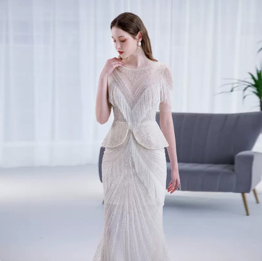 Woman wearing a white lace dress in a minimalistic room with a gray sofa and white curtains.