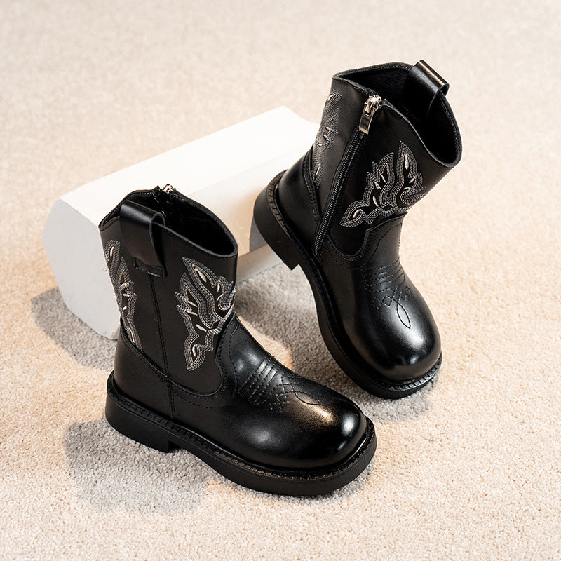 Black leather boots with decorative patterns on a beige surface