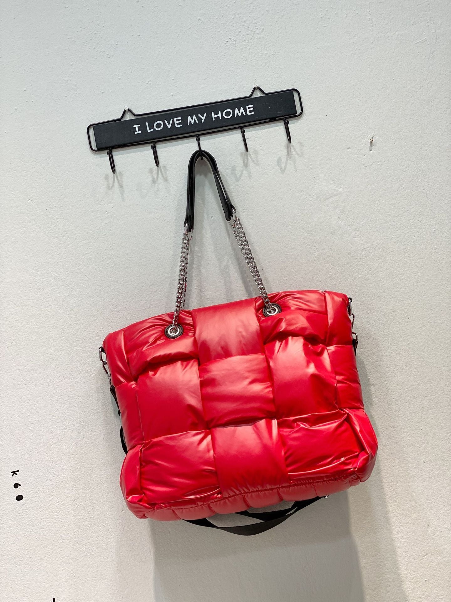Red puffer bag hanging on a wall hook with 'I Love My Home' sign.