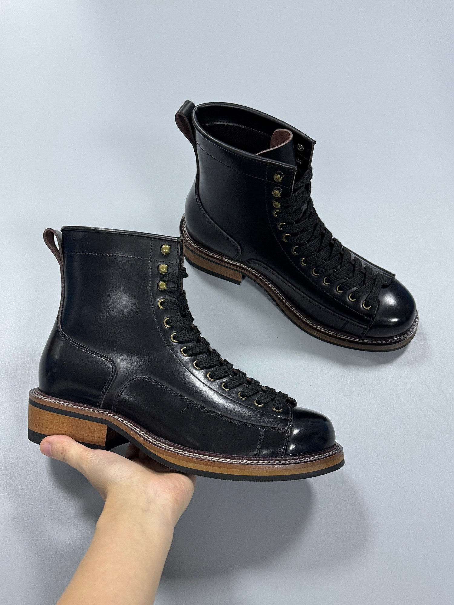 Pair of black leather boots with brown soles on a light gray background
