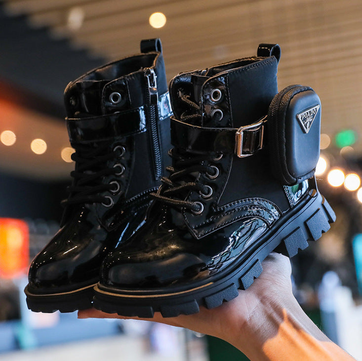 Black leather boots with decorative elements held in a hand against a blurred indoor background