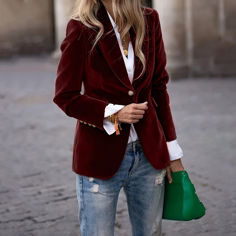 Person wearing a burgundy velvet blazer with a white shirt and blue jeans, holding a green handbag.