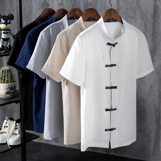 White short-sleeve shirt with black buttons on hangers against a gray wall.