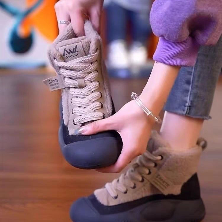 Person holding a gray shoe with a brand logo, wearing matching shoes on feet.