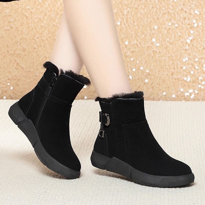 Black ankle boots with fur trim worn by a person on a neutral background